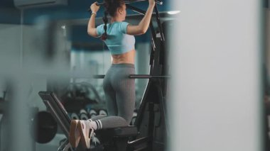 Atletik kadın destekli barfiks makinesinde sırt kasları için egzersiz yapıyor.