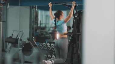 Sırtını ve kollarını güçlendirmek için bir makineye destek veren kararlı genç bir kadın.