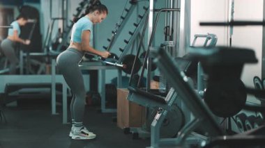 Azimli atletik kadın spor salonundaki bir kablo makinesine trisepsi itme egzersizi yapıyor.