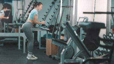 Modern bir spor salonunda egzersiz yaparken kollarını kablo makinesinde çalıştıran zinde bir kadın.