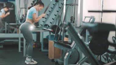 Spor salonunda yapılan yoğun bir egzersiz sırasında trisepslerini kablo makinesiyle çalıştıran atletik bir kadın.