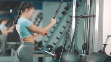 Spor salonundaki trisepsler için kablo makinesinde kas çalıştıran kadın.