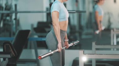 Odaklanmış zinde bir kadın halterle egzersiz yapıyor, ağırlık kaldırma egzersizleri yapıyor.