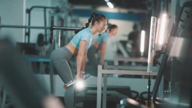 Genç atletik kadın modern bir spor salonunda Romanyalı dambılları kaldırıyor