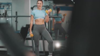 Atletik kadın antreman sırasında kol kaslarını dambıllarla çalıştırıyor.