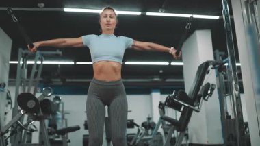 Güçlü bir kadın spor salonundaki kablo çapraz makinesinde göğüs ve omuz kaslarını çalıştırıyor.