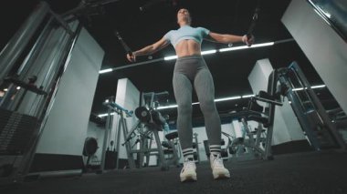 Atletik kadın modern bir fitness merkezinde kablo makinesinde göğüs sineği egzersizi yapıyor.