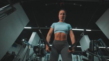 Kararlı atletik kadın modern bir spor salonunda bir kablo çapraz makinesinde göğüs egzersizi yapıyor.