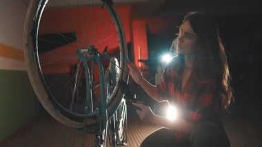 Loş ışıklandırılmış bir atölyede odaklanmış kadın tamirci ve antika bir bisiklet tekerleği bakımı