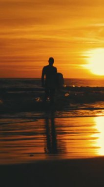 Gün batımında dalgalar içinde sörfçü bir adamın silueti. Orta çekim