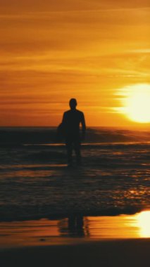 Gün batımında deniz dalgalarında sörfçü bir adamın silueti. Orta çekim