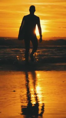 Günbatımının arka planında, okyanus dalgalarında, kaslı sörfçülerin silueti. Orta vuruş.