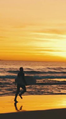 Gün batımında deniz kenarında sörf tahtası olan bir sörfçünün silueti. Orta vuruş.