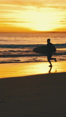 Gün batımında okyanus kıyısında sörf tahtası olan bir sörfçünün silueti. Orta vuruş.