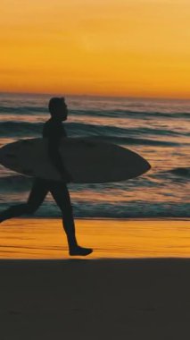 Gün batımında okyanus kıyısında sörf tahtası olan bir sörfçünün silueti. Orta vuruş.