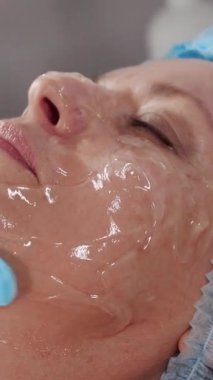 Kozmetik uzmanı kadın müşterinin yüzüne nemlendirici jel maske yayıyor.