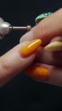 Tırnak sanatçısı, elektrikli oje kullanarak eski tırnak cilasını müşterinin parmağından çıkarıyor.