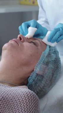 Kozmetoloji uzmanı. Kadın müşterisinin yüz derisini temizliyor. Orta çekim