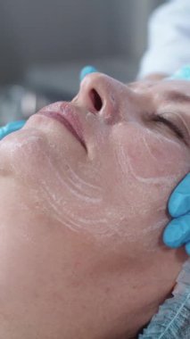 Kozmetoloji tedavisi. Kadın müşterisinin yüzüne masaj yapıp temizlik yapıyor. Orta çekim