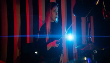 Genç bir kadın stüdyo ışıkları altında tutkulu ve yoğun bir konsantrasyonla davul çalıyor.