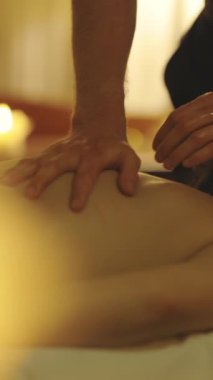 Masaj seansı. Bir terapistin erkek ellerine yakın çekim. Kadın bir müşterinin sırtını yağlıyor. Orta çekim