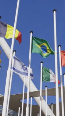 Parlak mavi gökyüzünün arkasındaki bayrak direğinde farklı ülkelerin bayrakları. Orta çekim