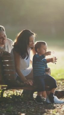 Ebeveynler, oğullarıyla bir bankta oturup sabun köpüğüyle oynuyorlar. Orta çekim