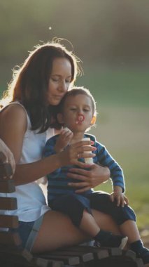 Ebeveynler bir bankta oturup oğullarını sabun köpüğüyle oynuyorlar. Orta çekim