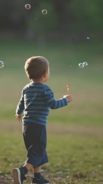 Parktaki küçük çocuk sabun köpüklerini yakalıyor ve kovalıyor. Orta çekim
