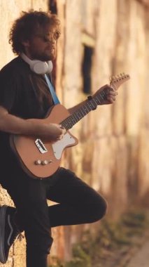 Duvarın yanında duran ve sokakta gitar çalan bir adam. Orta çekim