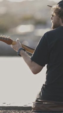 Şehrin seddindeki sette gitar çalan genç bir adamın arkasından görüntü. Orta çekim