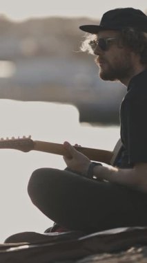 Şehirdeki toprak setinde gitar çalan genç bir adam. Orta çekim