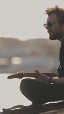 Rıhtımda gitar çalan bir erkek müzisyen. Orta çekim