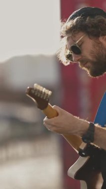 Sokaktaki duvarın yanında gitar çalan şık bir genç adam. Orta çekim