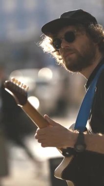 Gün batımında sokakta duvar kenarında gitar çalan bir adam. Orta çekim