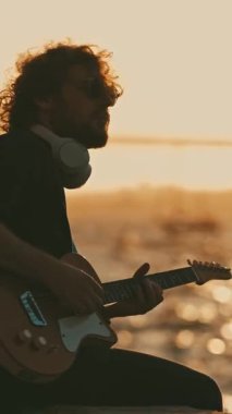 Genç bir adam gün batımında şehir setinde gitar çalar. Orta çekim