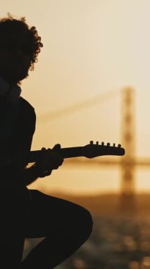 Gün batımında setin yanında gitar çalan bir adamın silueti. Orta çekim