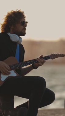 Yalnız stil sahibi bir adam setin yanında gitar çalıyor. Orta çekim