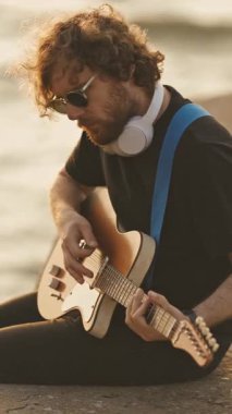 Şık, yalnız bir gitarist şehir setinde bacaklarını suya sarkmış oynuyor. Orta çekim