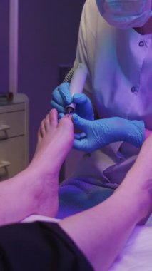 Usta, müşterisine mor ışıkta pedikür yapıyor. Orta çekim