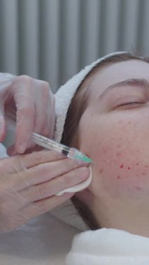 Derisi sorunlu bir kadının kozmetolojide randevusu var. Usta yanağına enjeksiyon yapıyor. Orta çekim