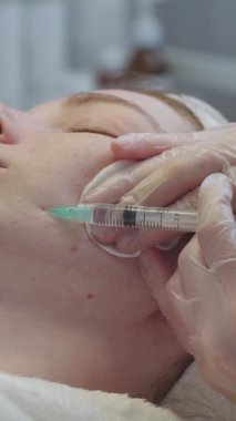 Derisi sorunlu bir kadının kozmetolojide randevusu var. Usta yanağına enjeksiyon yapıyor. Orta çekim