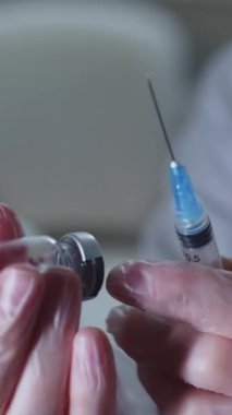 Bir sağlık çalışanı şişeden şırıngaya bir çözüm çizer. Orta çekim