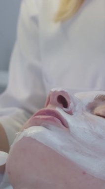Güzellik uzmanı bir fırça kullanarak müşterisinin yüzüne beyaz kalın bir maske takıyor. Orta çekim