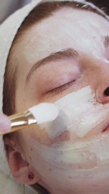 Kozmetik uzmanının cilt bakımı. Usta, müşterilerin yüzüne fırçayla beyaz maske takıyor. Orta çekim