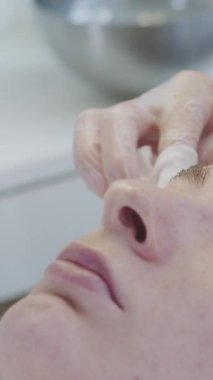 Bir güzellik uzmanı, genç bir bayan müşterinin çilli yüzünü peçetelerle siliyor. Orta çekim