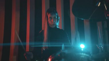 Ses geçirmez bir odada kırmızı ve mavi ışıkları olan davul çalan genç bir kadın.