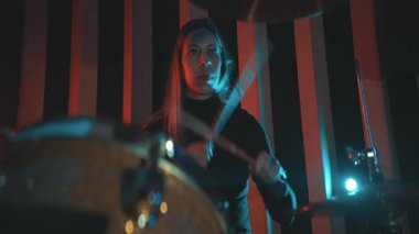 Karanlık bir stüdyoda canlı performans sırasında tutku ve enerjiyle davul çalan bir kadın.