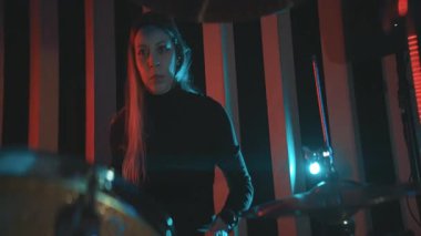 Konsantrasyonu olan genç bir kadın karanlık bir stüdyoda müzik performansı sırasında davul çalıyor.