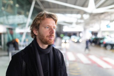 Arka planda bulanık arabalarla havaalanı terminalinde dikilen bir adam.